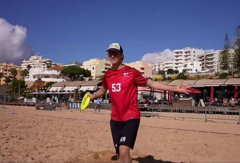 Frisbeespieler auf Sand, der eine Scheibe gefangen hat und sich freut